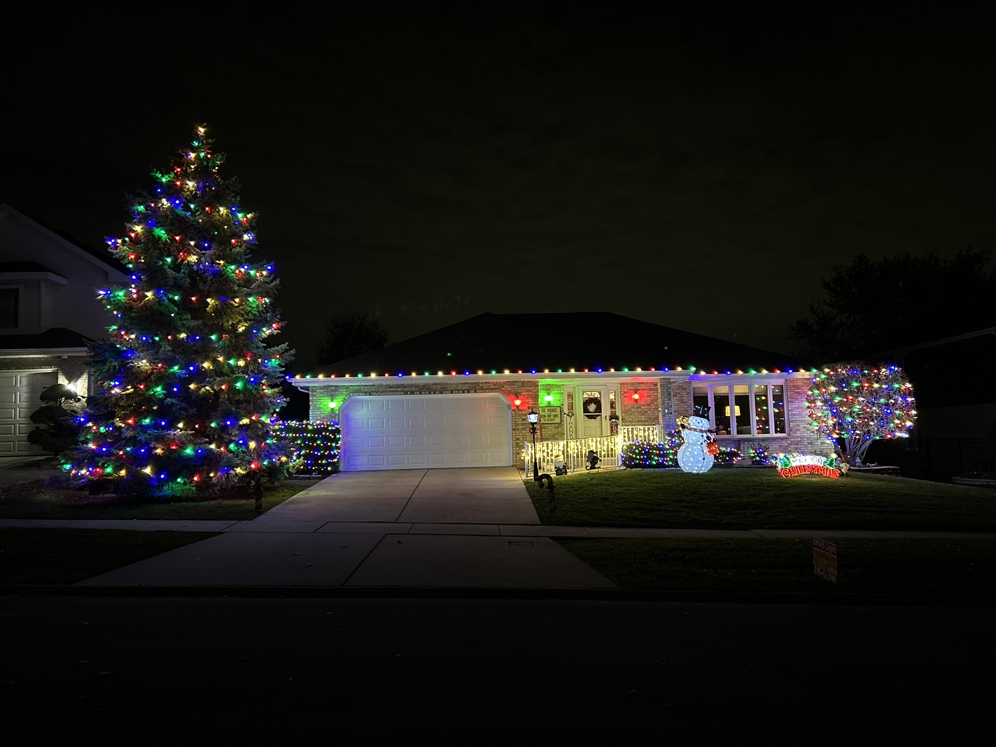 Home with multicolor roofline lights and a large multicolor lit evergreen